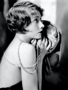 an old black and white photo of a woman with pearls on her neck, looking off to the side