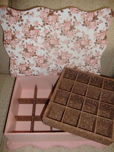 a pink box filled with chocolate squares next to a piece of cake on top of a table