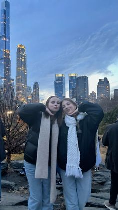 two women are posing for the camera in front of a cityscape at dusk