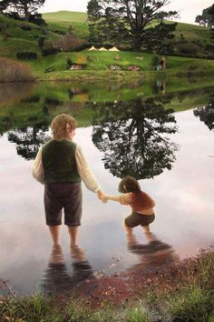 a woman holding the hand of a child near a lake