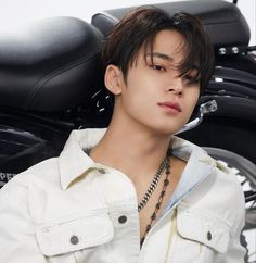 a young man sitting in front of a motorcycle wearing a white shirt and black necklace