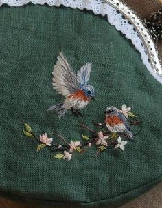 two birds sitting on top of a green bag with flowers and leaves embroidered on it