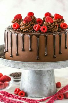 a chocolate cake with raspberries and chocolate icing on a silver platter