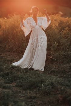 a woman wearing a white dress standing in a field with her hands up and smiling