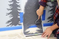 a woman is painting a wall with black paint and pine trees on the walls behind her