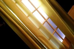 an open window with yellow curtains and light coming through it