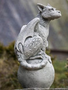 a statue of a dragon sitting on top of a stone ball in front of some bushes