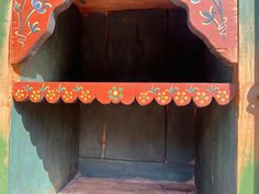 an old wooden shelf with painted designs on it's sides and wood door in the background