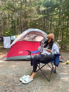 a woman sitting in a chair next to a tent with a cup on her lap