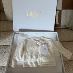 a baby's white cardigan in a box with the name dior on it