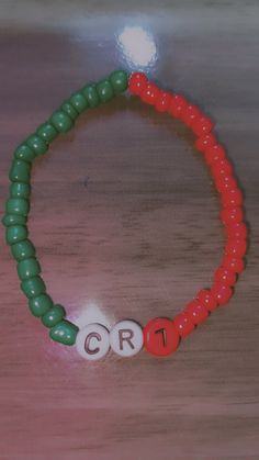 a red and green beaded bracelet with the word crt on it, sitting on a wooden table