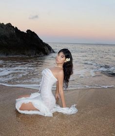 a woman in a white dress sitting on the beach