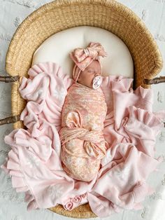 a newborn baby wrapped in pink is laying on a wicker basket with ruffles