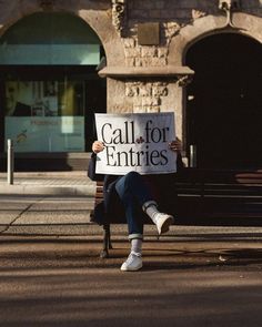 a person sitting on a bench with a sign that says call for entries in front of them