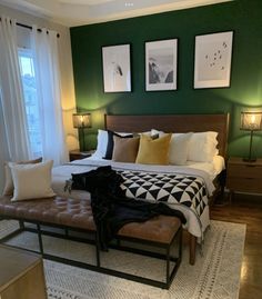 a bedroom with green walls and pictures on the wall above the bed, along with an ottoman