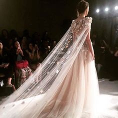 a woman is walking down the runway in a dress with flowers on it and veil over her head