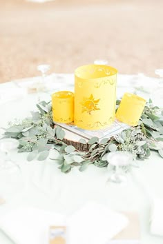 two yellow candles sitting on top of a table with greenery and flowers around it