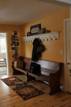 a wooden bench sitting on top of a hard wood floor next to a wall mounted coat rack