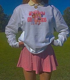 a woman standing in the grass with her hands on her hips wearing a white sweatshirt and pink skirt