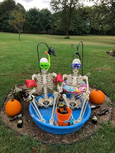 two skeleton statues sitting on top of a blue pool filled with halloween decorations and drinks