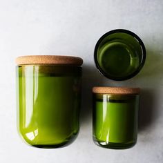 two green jars with lids sitting next to each other on a white surface, one is filled with liquid and the other has a cork lid