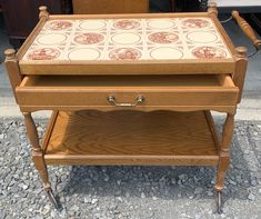 an antique wooden table with tile top and two drawers on wheels, in the middle of graveled area