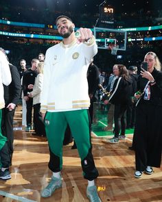 a man standing on top of a basketball court wearing green sweatpants and a white jacket