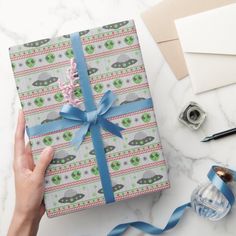 a hand holding a wrapped present on top of a table next to blue ribbon and other items