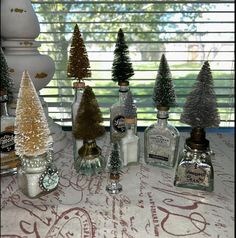 bottles filled with different types of christmas trees on a table next to a window sill