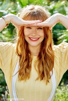 a woman with long red hair is holding her hands over her head and smiling at the camera