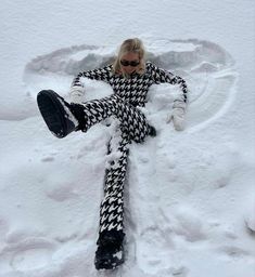 a woman laying in the snow with her legs spread out and wearing black and white checkered pants