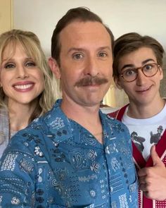 three people standing next to each other in front of a mirror with the man's moustache visible