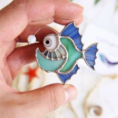 a hand holding a blue and green fish brooch