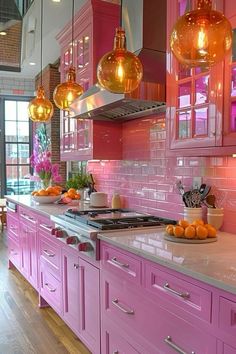 a kitchen with pink cabinets and lights hanging over the stove top, along with oranges on the counter