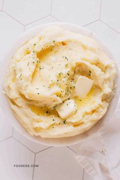 mashed potatoes with butter and herbs in a white bowl on a white tablecloth