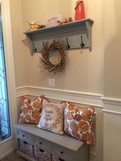 a bench with some pillows on it in front of a window and a wreath above the bench