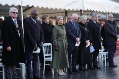 a group of people standing next to each other in front of a tent on a rainy day