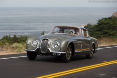 an old car driving down the road by the ocean