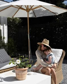 a woman holding a baby sitting on top of a wicker chair next to an umbrella