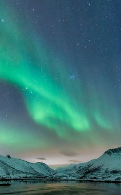 the sky is filled with green and blue aurora bores above snow covered mountains in iceland