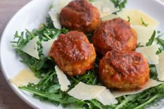 three meatballs with parmesan cheese and greens on a plate