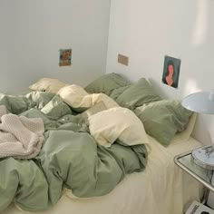 an unmade bed with green sheets and blankets on it, next to a lamp