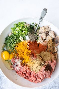 a bowl filled with meat, seasoning and spices on top of a white table