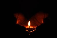 two hands holding a lit candle in the dark