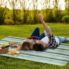 two people laying on a picnic blanket in the grass with food and drinks laid out around them