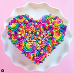 a heart shaped cake on a white plate with sprinkles and rainbow colors