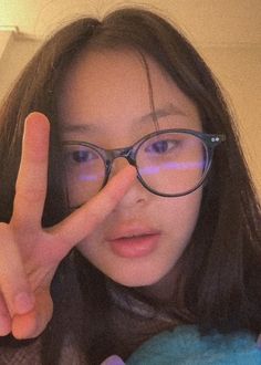 a woman wearing glasses making the v sign with her fingers