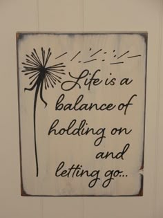 a wooden sign that says life is a balance of holding on and letting go with dandelions