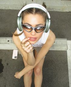 a woman wearing headphones and sunglasses leaning on a bench