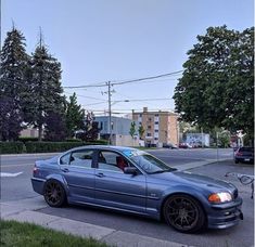 a blue car parked on the side of a road next to a tree filled street